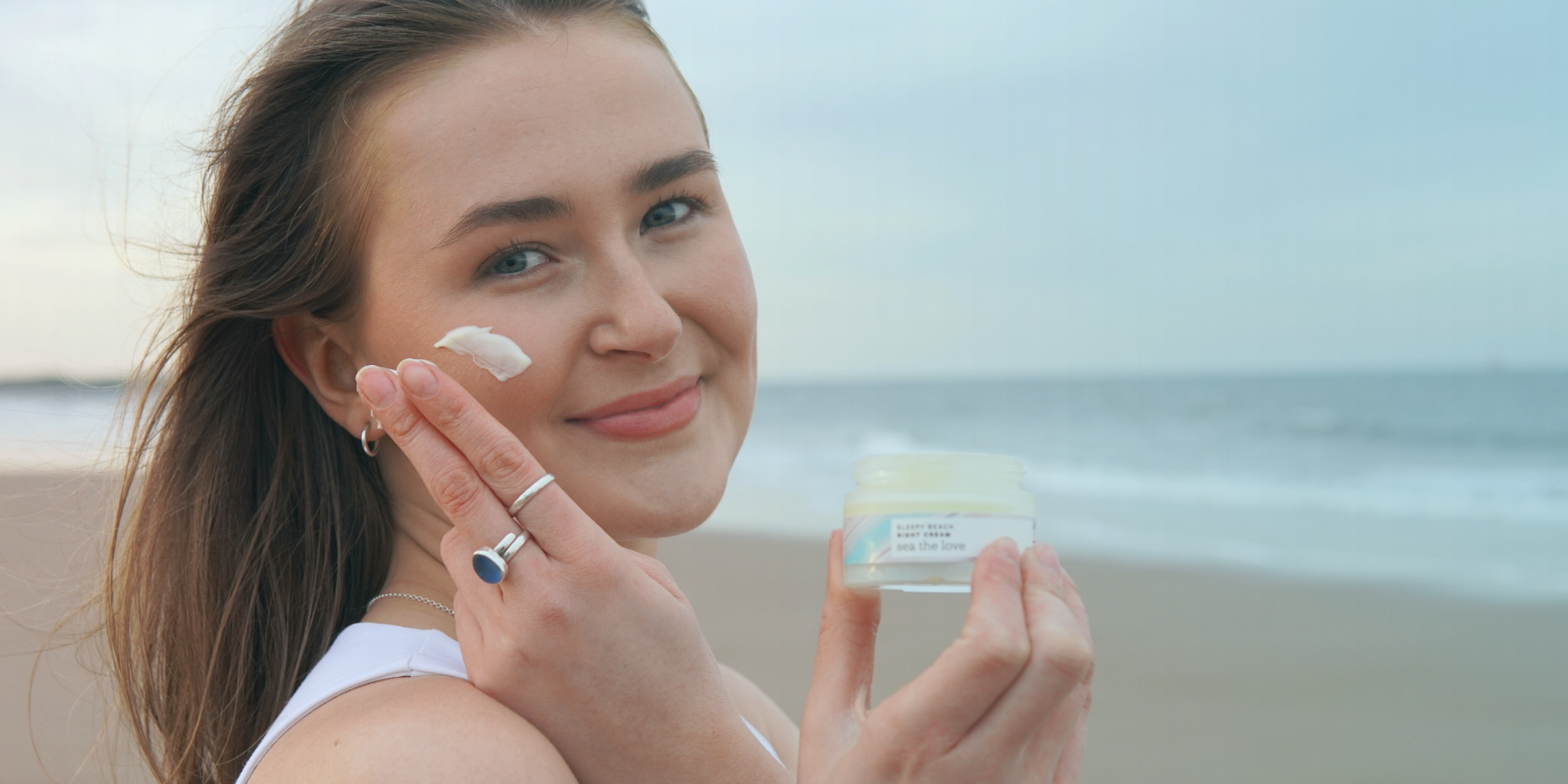 Woman applying night cream on the beach with a jar of night cream in hand