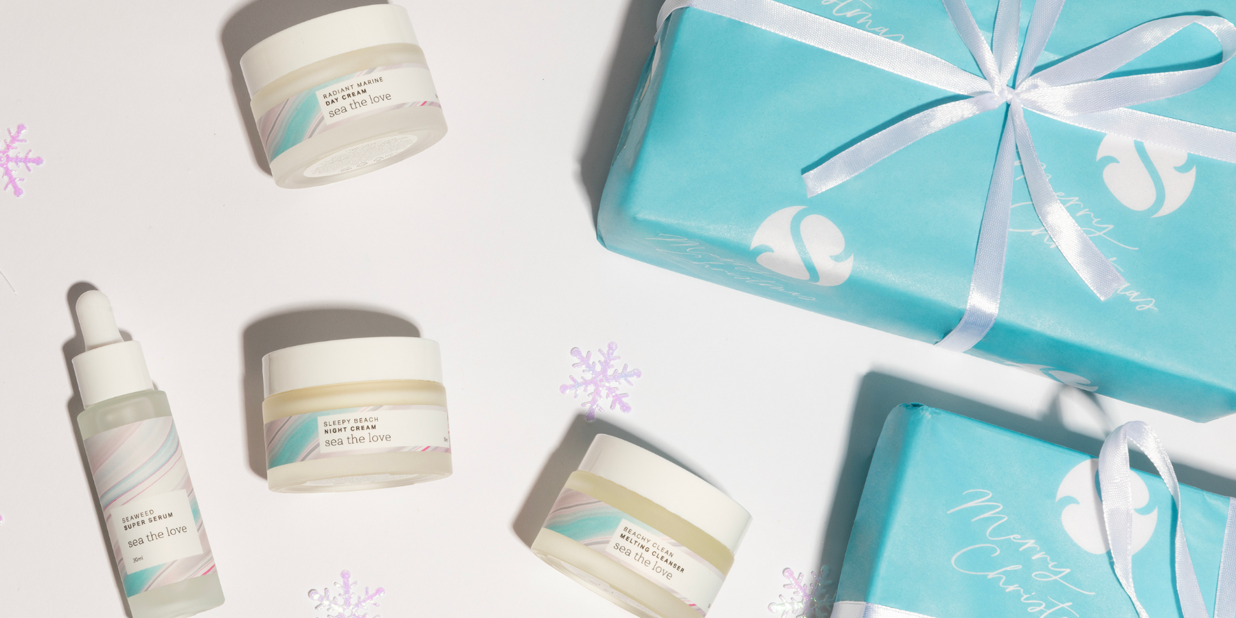 Skincare products including jars and a bottle with blue Christmas gift boxes on a white background