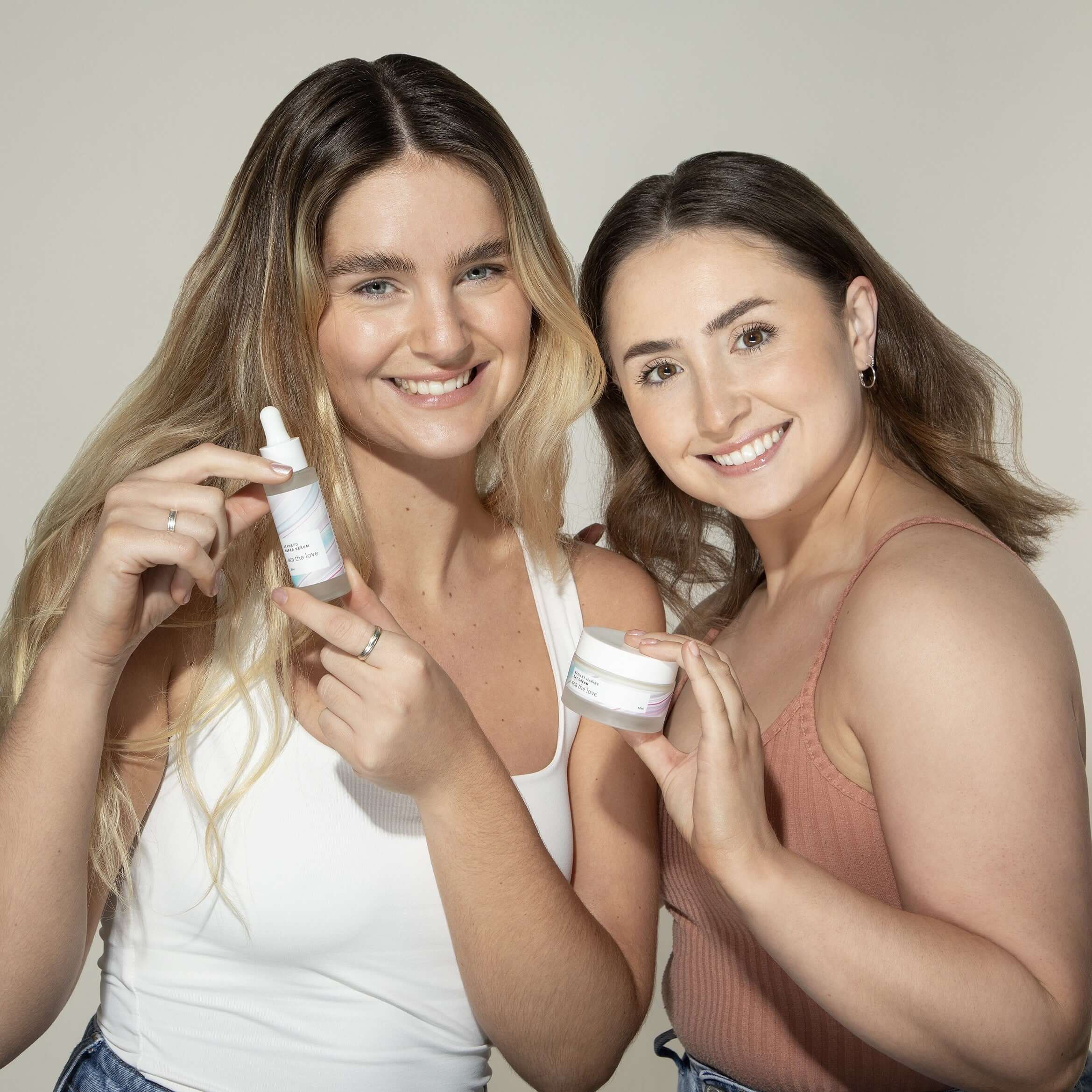 Two smiling women holding Sea the Love ocean skincare products, including a seaweed serum and marine moisturiser.
