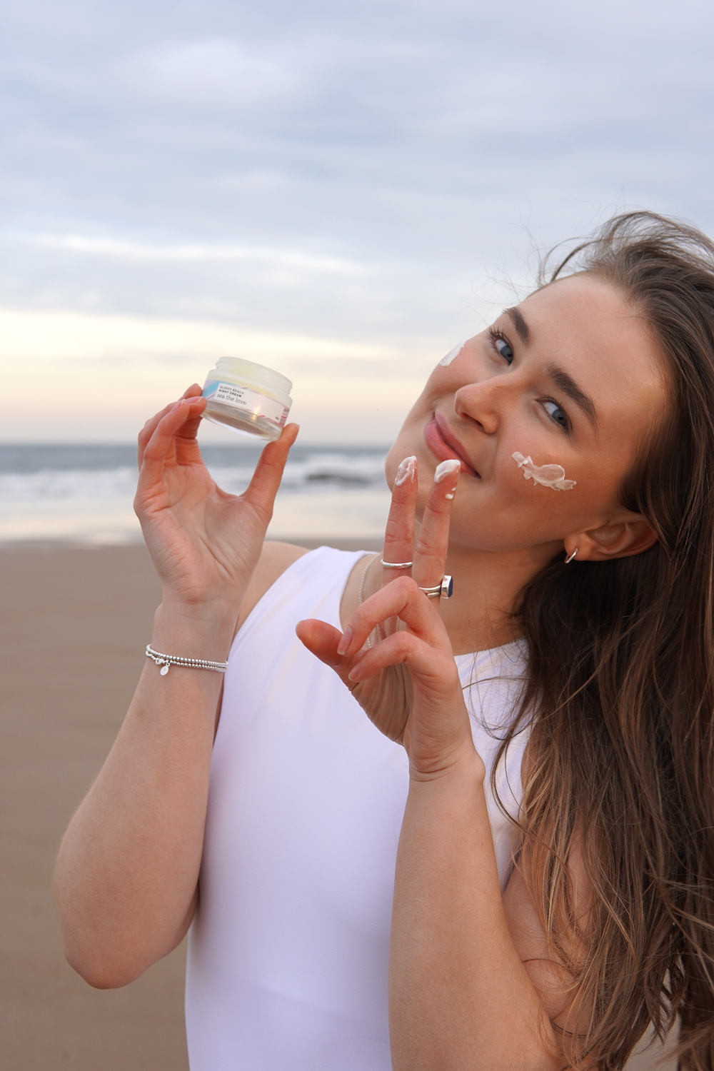 A woman stands on a beach, smiling as she holds a jar of algae night cream. The image highlights the benefits of ocean-based skincare, emphasizing the moisturizing properties of the algae-infused product.
