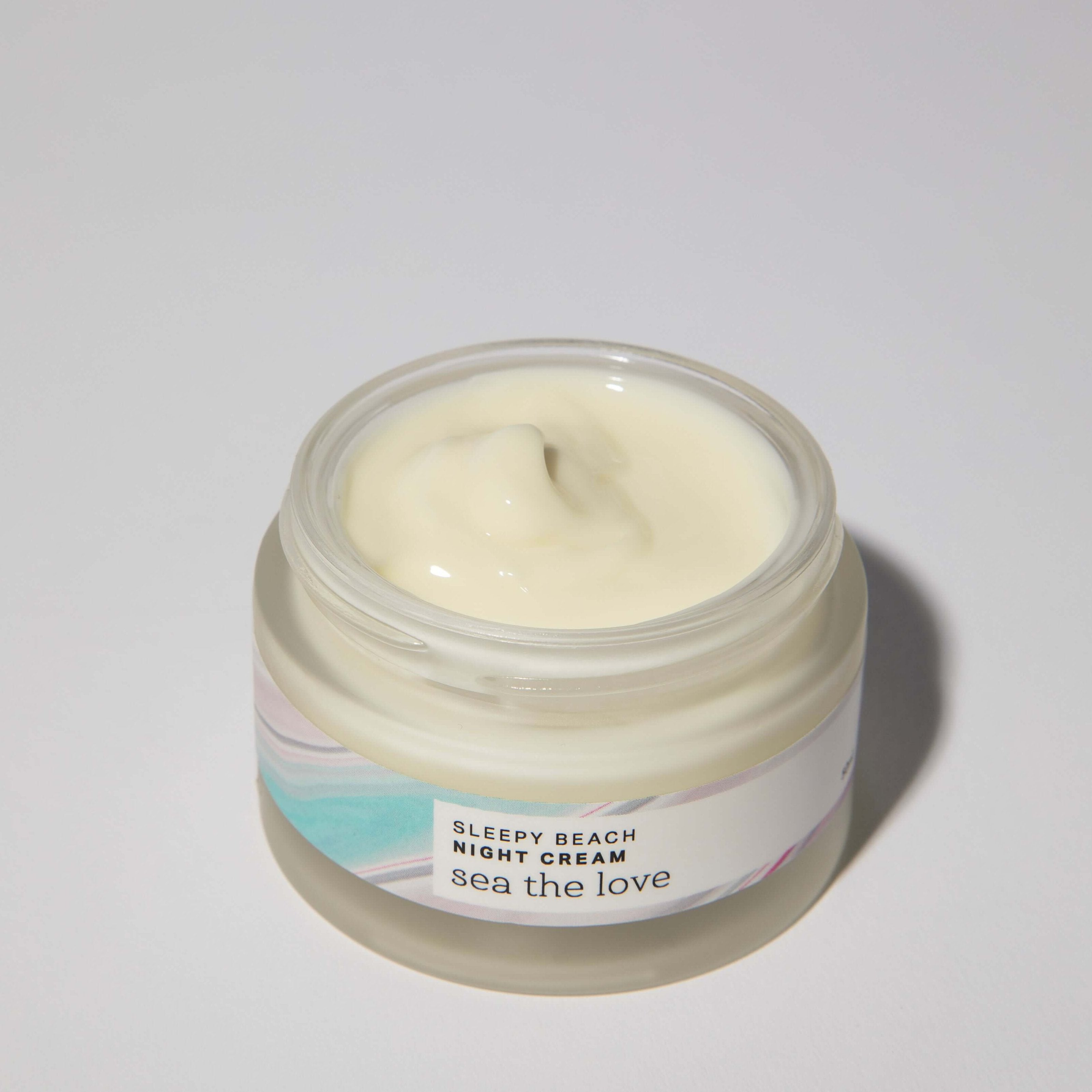  A open jar of Sleepy Beach Night Cream, showcasing its creamy texture, infused with sea minerals and green microalgae.