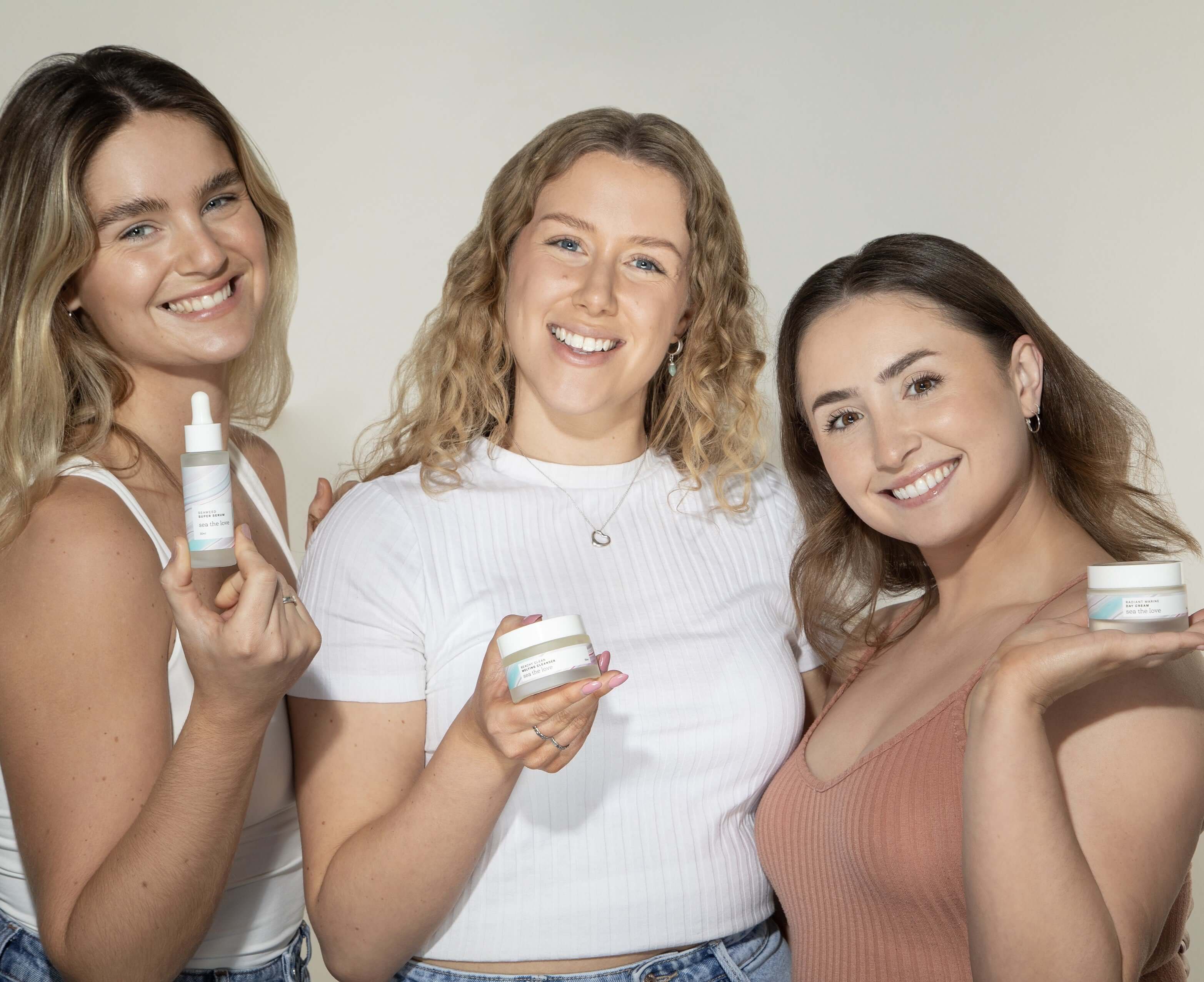 Three women smiling holding an ocean inspired skincare product from sea the love, infused with sea minerals for healthy skin. 