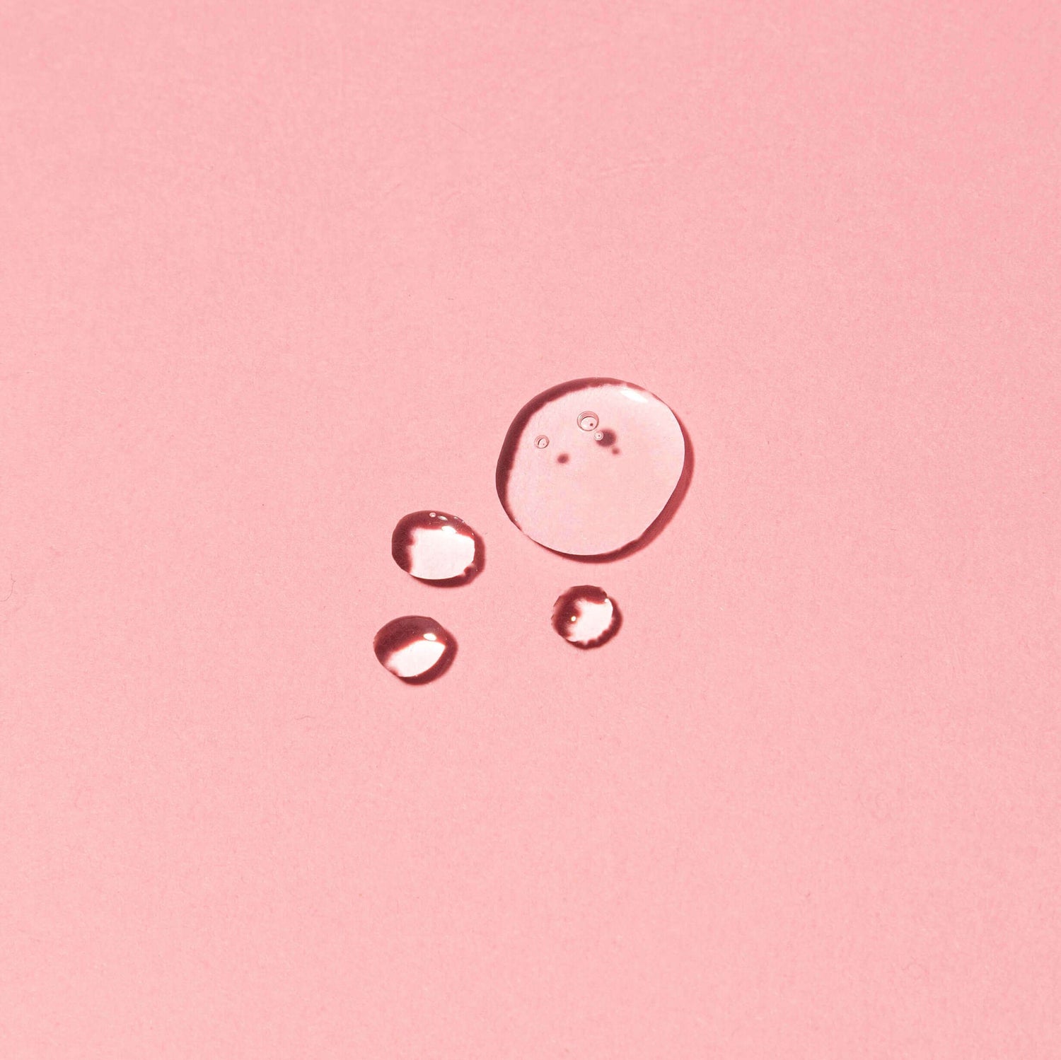 Close-up of Seaweed Super Serum drops on pink background showcasing consistency of the hydrating seaweed serum formula with natural ingredients.