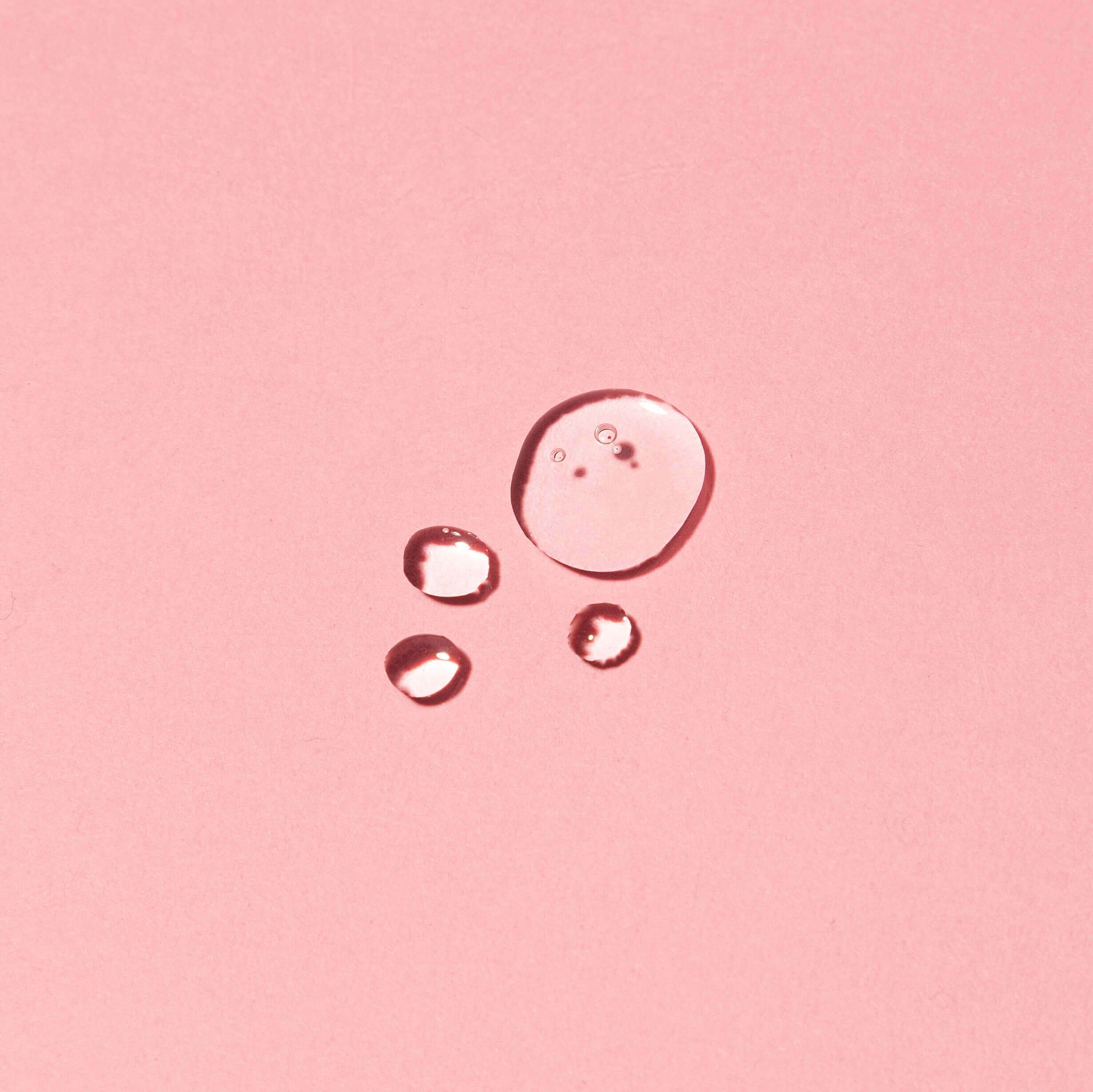 Close-up of Seaweed Super Serum drops on pink background showcasing consistency of the hydrating seaweed serum formula with natural ingredients.