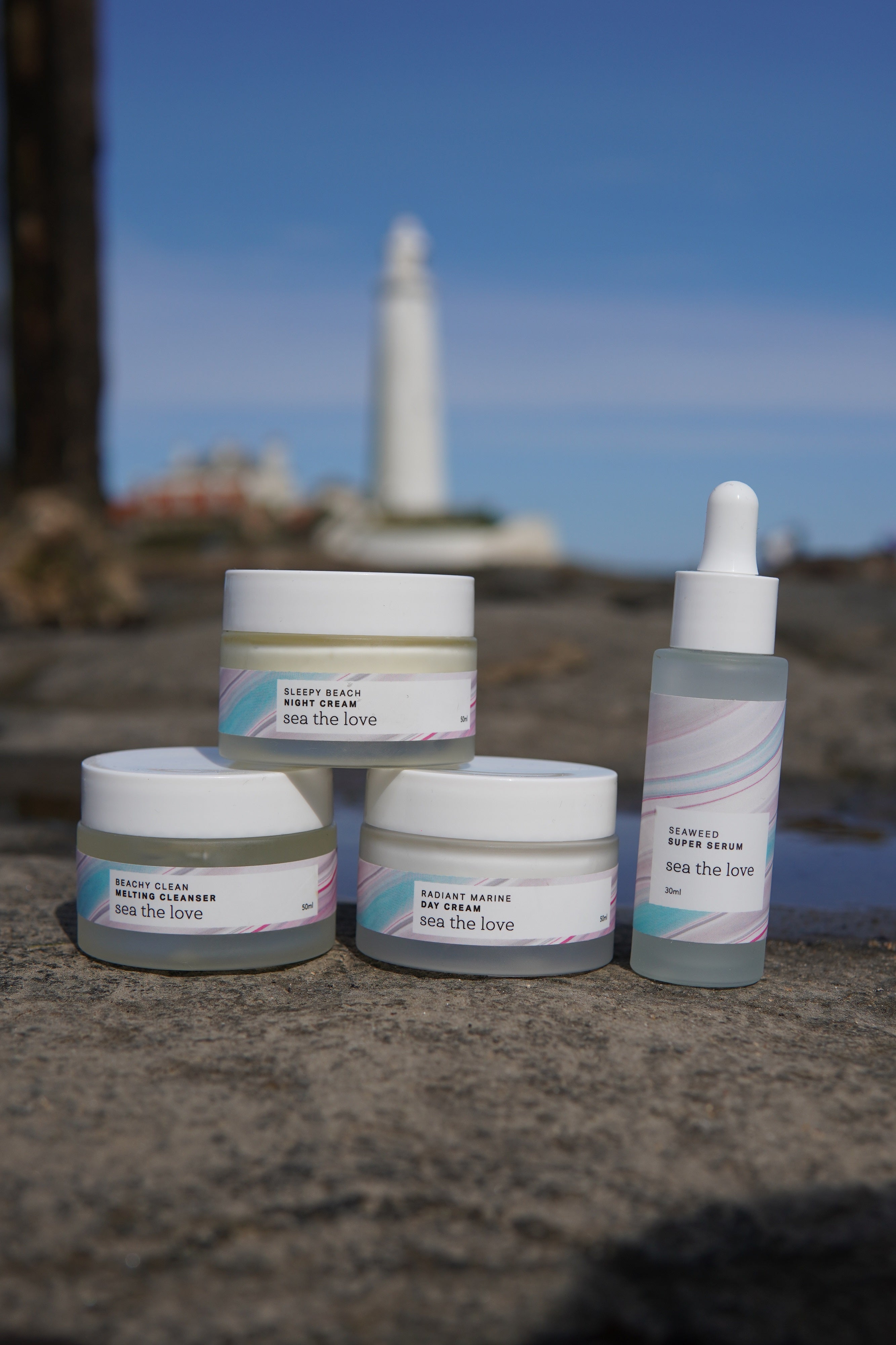 Sea the Love's full range of ocean inspired skincare products consisting of a serum, cleanser, night cream and day cream, pictured in front of St Marys lighthouse in Whitley Bay